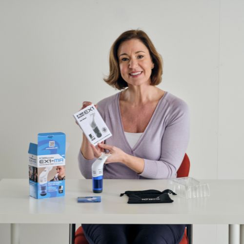 Person seated at a table holding a boxed breathing training device, with the device and accessories displayed.